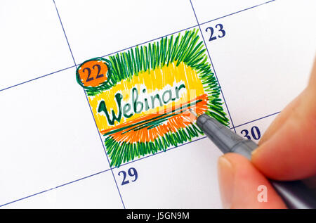 Dita di donna con penna scrittura Webinar promemoria nel calendario. Foto Stock