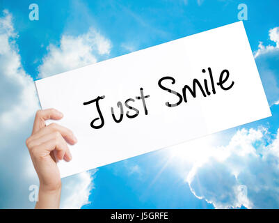 Just Smile segno su carta bianca. Man mano che tiene la carta con testo. Isolato su sfondo cielo. Il concetto di business. Stock Photo Foto Stock