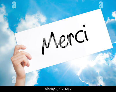 Merci (grazie in francese) firmare su carta bianca. Man mano che tiene la carta con testo. Isolato su sfondo cielo. Il concetto di business. Stock Photo Foto Stock