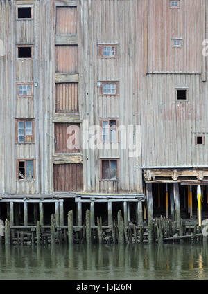 Un antico magazzino di legno in piedi su pali di legno sulla riva del fiume Nidelva. Trondheim, Sør-Trøndelag, Norvegia. Foto Stock