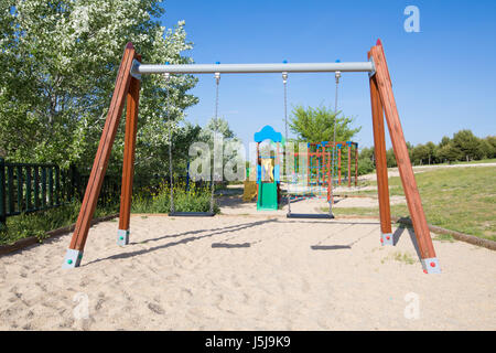 Plastica due insiemi di oscillazione sulla terra la massa di sabbia nel parco giochi con scivolo nel parco pubblico Stazione di depurazione di Valdebebas nella città di Madrid, Spagna Europa Foto Stock