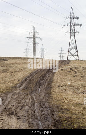Sporco strada rustico con tracce dal trattore accanto a linee di alimentazione. Foto Stock
