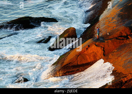 La mattina presto in Niemayer Avenue, un pescatore di provare la sua fortuna sulle rocce sotto, vicino al mare. Foto Stock