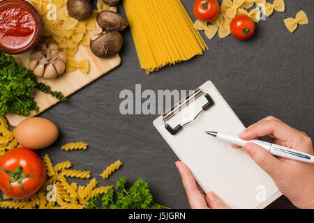 Italiano Foto di spaghetti ricetta. Mano con la scrittura della penna su carta bianca sul tavolo di cucina circondato con prodotti. Foto Stock