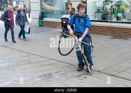 Un giovane locale competente consiglio lavoratore utilizzando una macchina per soffiare la gomma da masticare off i marciapiedi in Canterbury centro citta'. Foto Stock