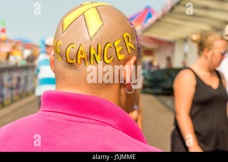 Bald donna con la scrittura sul suo capo cercando di raccogliere fondi per beneficenza a Herne Bay pier, Kent, Inghilterra, Regno Unito. Foto Stock