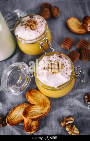 Frullato di zucca in un barattolo di vetro con la panna montata, caramella mou, noce e miele biscotti. Bottiglia di latte. Tovagliolo grigio. Sfondo. Il fuoco selettivo. Foto Stock