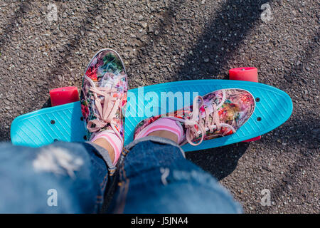 In prossimità dei piedi di una ragazza in rosa sneakers corse su blue penny skateboard con ruote di colore rosa. Scena urbana, la vita della città. Sport e fitness stile di vita. Foto Stock