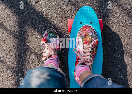 In prossimità dei piedi di una ragazza in rosa sneakers corse su blue penny skateboard con ruote di colore rosa. Scena urbana, la vita della città. Sport e fitness stile di vita. Foto Stock