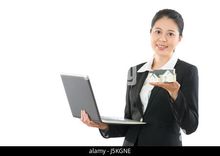 Gentile lavoratore di ufficio lady holding che mostra in miniatura Modello di casa mobile e il computer portatile di lavoro on-line con il client da ovunque sul copyspa Foto Stock