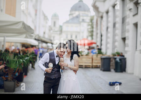 Sposa e lo sposo a piedi lungo una città solare e mangiare il gelato Foto Stock