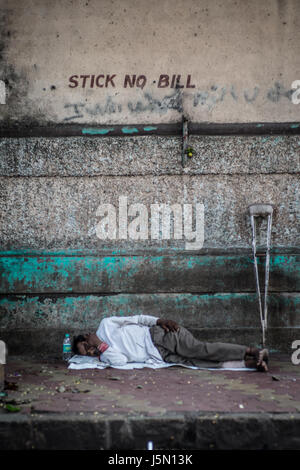 Un uomo dorme durante il pomeriggio caldo accanto ad una parete in una strada a Mumbai, India Foto Stock