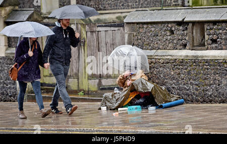 Brighton, Regno Unito. 18 Maggio, 2017. Un uomo chiede soldi sotto un ombrello sul marciapiede come la gente a piedi passato sotto una pioggia torrenziale nel centro di Brighton oggi Credito: Simon Dack/Alamy Live News Foto Stock