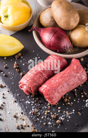 Foto verticale con rulli di carni bovine. Due sottili fette di rosso la carne cruda preparata per involtino. Cibo su ardesia nera pietra con campana gialla peperoni cipolla, materie p Foto Stock