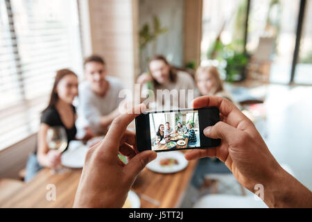 Primo piano dell'uomo a scattare foto di suoi amici con un telefono cellulare di mangiare al tavolo a casa Foto Stock