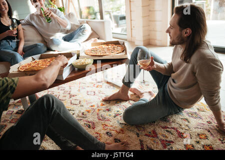 Rilassata attraente giovane uomo di bere vino e mangiare la pizza con gli amici a casa Foto Stock