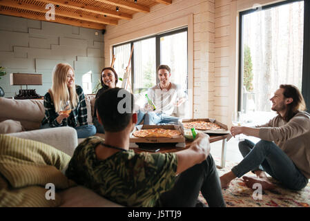 Un gruppo di giovani felici hanno mangiare la pizza e rilassarsi nel salotto di casa Foto Stock