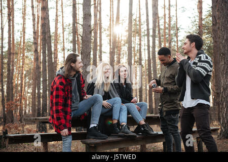 Foto di gruppo sorridente di amici seduti all'aperto nella foresta. Cerca riposo e parlare. Foto Stock