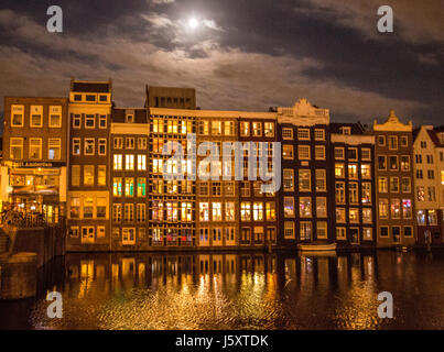 Luna piena sopra l'illuminato di canali di Amsterdam e case durante la notte, con riflessioni sull'acqua. Foto Stock