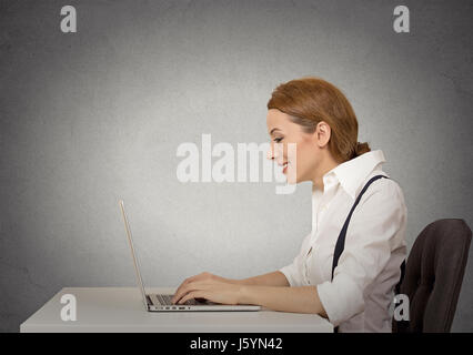 Vista laterale attraente profilo happy business Donna che utilizza il suo computer portatile isolato muro grigio Sfondo. Corporate executive lavorando sul computer, lavori di posa in opera in corrispondenza di h Foto Stock