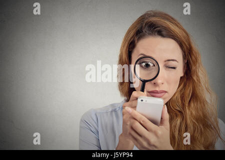 Curioso. Business donna guardando attraverso la lente di ingrandimento su smart phone schermo isolato uno sfondo grigio. Volto umano espressione. Investigatore ricerca Foto Stock