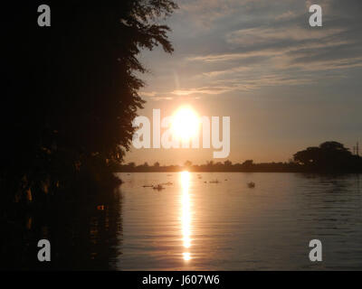 Questa immagine raffigura il tramonto sui distretti del fiume Pampanga nelle Filippine, in particolare a San Juan, Santa Cruz e Pambilog a San Luis. La pittoresca scena cattura l'atmosfera serena del fiume al crepuscolo. Foto Stock