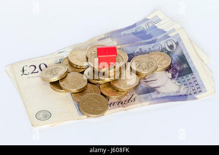 Un piccolo modello di plastica casa rossa sulla sommità di una pila di libbra di monete. Finanziamento di alloggi, proprietà o finanza immobiliare di concetto. Foto Stock