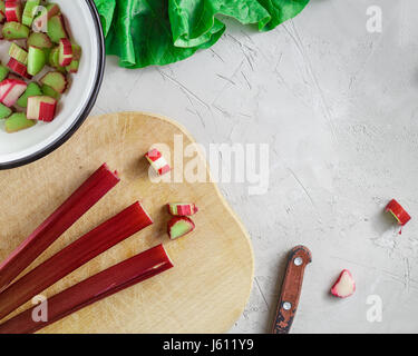 Fresche biologiche degli steli di rabarbaro sul tagliere di legno su cemento grigio sfondo di pietra Foto Stock