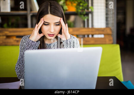 Giovane donna che lavorano in ufficio escursioni nella parte anteriore del computer portatile che soffrono di malattie croniche quotidianamente il mal di testa Foto Stock