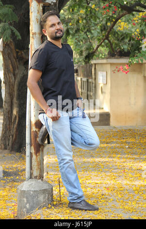 Giovane uomo indiano in appoggio contro il palo della luce su un lato strada Foto Stock