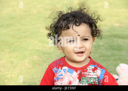 Piccola e dolce bambino con capelli ricci cercando e sorridente Foto Stock