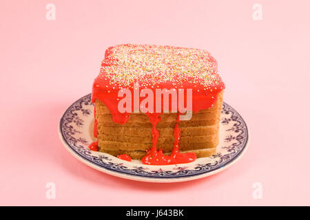 Un eccentrico ciliegina compleanno pane ricoperte con un pizzico di colore rosso e il coulis su sfondo rosa Foto Stock