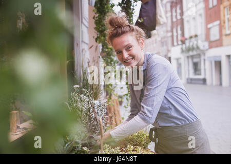 Ritratto sorridente giovane femmina fioraio disponendo display in vetrina Foto Stock