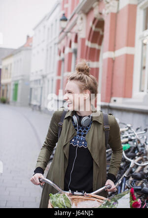 Sorridente giovane donna con cuffie equitazione Bicicletta su una strada di città Foto Stock