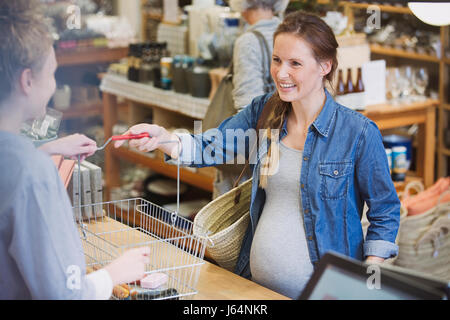 Donna incinta dando carrello alla cassa presso la cassa in negozio Foto Stock