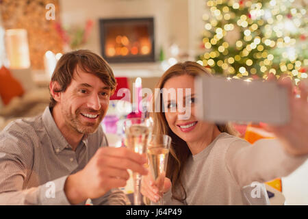 Coppia sorridente tostare champagne flauti e tenendo selfie a cena di Natale tabella Foto Stock