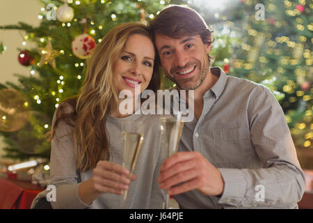 Ritratto sorridente giovane tostatura flauti champagne nella parte anteriore dell albero di Natale Foto Stock