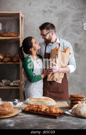 L'immagine verticale di un felice fornai che abbraccia e cercando di ogni altro nel forno mentre l uomo sacco di contenimento con pane Foto Stock