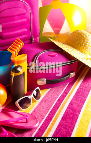 Vacanze estive con uno sfondo con borsa rosa, crema solare, flip-flop e giocattoli da spiaggia. Foto Stock