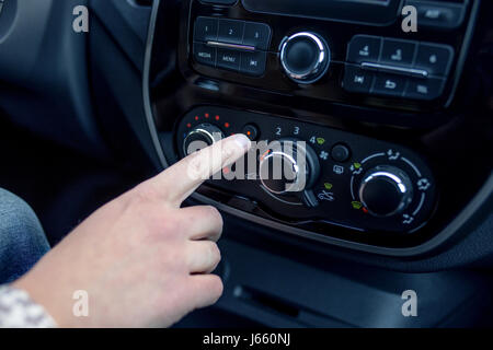 Maschio lato premendo il pulsante in auto moderna. L'uomo regola la temperatura della vettura il condizionatore d'aria Foto Stock