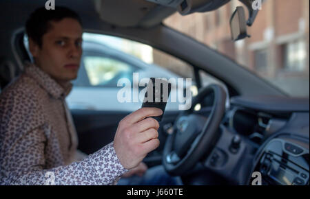 Uomo che guarda fuori dalla finestra di auto e trattenimento di un antifurto per auto chiave. Uomo effetto di sfocatura. Foto Stock
