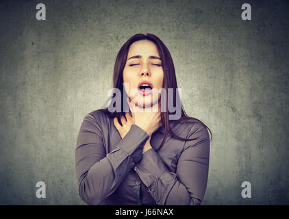 Giovane donna avente attacchi di asma o parzializzando non respiro che soffre di problemi respiratori isolati su sfondo grigio Foto Stock