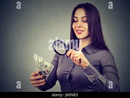 Giovane donna guardando banconote da cento dollari attraverso la lente di ingrandimento Foto Stock