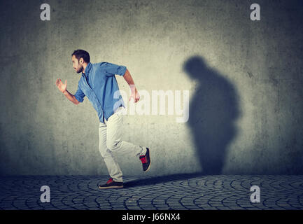 Uomo che corre lontano dal suo triste cupo fat ombra sul muro. Salute mentale e controllo del peso corporeo concept Foto Stock