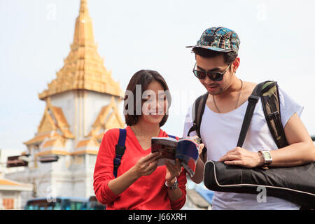 Coppie di giovani asiatici viaggia l uomo e la donna la lettura messaggio nella guida del viaggiatore prenota con felicità faccia contro il tempio pagoda in Thailandia Foto Stock