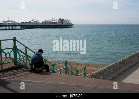 Giovane uomo controllo telefono sulla scalinata che conduce alla spiaggia, Brighton, Regno Unito Foto Stock