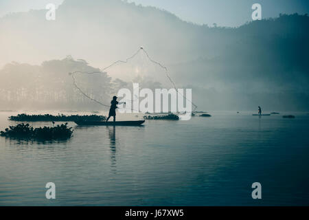 Fisherman gettata la sua rete da pesca nel fiume da gettando in alto in aria presto nel colore blu mattina per la cattura del pesce con la sua piccola Foto Stock