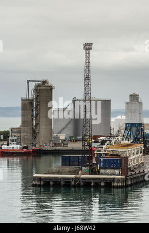 Napier, Nuova Zelanda - 9 Marzo 2017: Grandi serbatoi di carburante e silos a porto commerciale sotto il cielo d'argento. Rimorchiatore, pali della luce, contenitori e altri ha Foto Stock