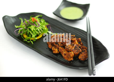 Brasato di manzo con salsa di peperoncino, seasame e insalata sul piatto nero Foto Stock