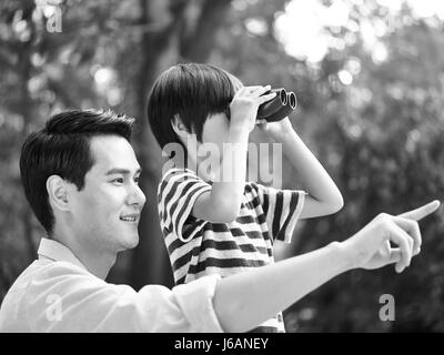 Asian padre e figlio con il binocolo nel parco, in bianco e nero. Foto Stock